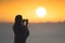 Silhouette of woman with wet hair wrapped in a blanket after swimming. Female taking picture on mobile phone standing on the beach