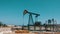 Silhouette of working oil pump and an old rusty iron barrel near on a background of blue sky and clouds.Oil pumpjacks in