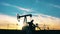 Silhouette of a working oil pumpjack in an oil field at sunset