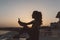 Silhouette of young attractive woman in sportswear making selfie on seafront on sunset background. Expressing positivity