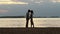 Silhouette of a young couple in love at sunset. Girl stood on tiptoe and gently kisses the guy on the shore of the lake