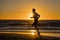 Silhouette young dynamic athlete runner man with fit strong body training on Summer sunset beach running barefoot in sport healthy