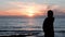 Silhouette of young girl looking at sunset. Attractive girl in casual wear standing on rocky shore and looking at ocean. Silhouett