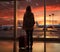 Silhouette of a young girl with a suitcase standing at the airport window. The evening light of sunset. Generated by AI.