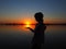 Silhouette of a young girl on a sunset background. The child holds the setting sun on her hand. Horizon, water, sun and