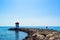 Silhouette of a young guy on the stones of the breakwater,  by the end of which stands a lighthouse