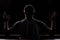 Silhouette of a young guy who sits in church and praying with hands raised up. Close-up view from behind. Backlight