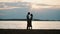 Silhouette of young happy couple hugging on the shore of the river in evening. Man and woman spending time on the beach.