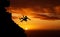 Silhouette of a young male hiker abseiling down the side of a mountain backlit against a sunset sky. Active and sporty