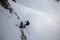 Silhouette of young man abseiling down from a snowy cliff. Climber rappelling from a white rock