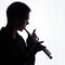 Silhouette. A young man is playing the flute. A square picture. Copy space.