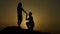 Silhouette of young man proposing to girlfriend on his knee, romantic engagement