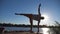Silhouette of young man standing at yoga pose on a wooden jetty at lake. Sporty guy training at nature. Athlete doing