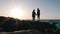 Silhouette of young romantic couple stands on beach at sunset. Man holds his beloved woman hand, talking to her and showing smth i