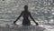 The silhouette of the young slender happy woman who stand in the sea and splashes water hands.slow motion