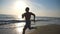 Silhouette of young sporty man running fast along coast during sunrise. Athletic boy training on sea beach. Male