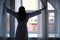Silhouette of young woman in bathrobe in hotel near the window in morning.