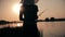 Silhouette of young woman in hat resting on nature fishing on a fishing rod by spinning at dawn