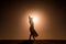 Silhouette of young woman with long skirt dancing in evocative and confident way on top of desert dune at sunset with sun high in