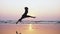 Silhouette of young woman performing grand jete jump on the beach in slow motion