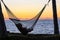 Silhouette of a young woman resting in a hammock and watching sunset over Pacific ocean