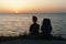 Silhouette of young woman sitting on the seashore with a backpack on the sunset background