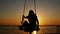 Silhouette of young woman swinging on a swing through the sun at beautiful sunset on tropical beach. slow motion