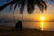 Silhouetted couple in love walks on the beach during sunset. Riding on a swing tied to a palm tree and watching the sun go down