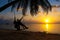 Silhouetted couple in love walks on the beach during sunset. Riding on a swing tied to a palm tree and watching the sun go down