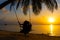 Silhouetted couple in love walks on the beach during sunset. Riding on a swing tied to a palm tree and watching the sun go down