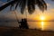 Silhouetted couple in love walks on the beach during sunset. Riding on a swing tied to a palm tree and watching the sun go down