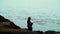 A silhouetted fisherman gets a strong catch on a rocky beach ledge