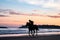 A silhouetted horse rider galloping across a beach at sunrise
