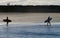 Silhouetted Male Surfers Carrying Surfboards into Pacific Ocean.