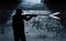 A silhouetted man is seen firing a gun in a dark spot under an overpass in a city