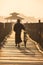 Silhouetted man walks bike along wooden footbridge