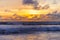 Silhouetted surfers on the waves and clouds in the bright colored sky during sunset. Evening on a tropical beach.