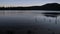 Silhouetted trees reflect in glassy lake during sunrise.