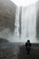 Silhouetted woman in jacket looking at breathtaking Skogafoss Waterfall in Iceland