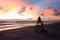 A silhouetted woman taking a picture of the sea on top of a lifeguard tower on a beach with the sun rising.