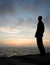 Silhouetted young man watches sunrise from a pier.