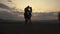 Silhouettes of athletic muscular couple of fitness instructors posing on sunset on the mountain peak. Beautiful cloudy