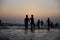 Silhouettes of children jumping in the surf on the background of the sea and evening sky. Boyish figures, children playing on