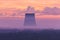 The silhouettes of the cooling towers of thermal power station among the forest on the background of scarlet sunrise or sunrise