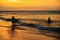 Silhouettes of couple of young surfers with surfboards walking on the beach in sunset