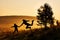 Silhouettes of a daughter and father making happy jump during beautiful golden sunrise. Foggy landscape in the mountains