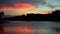 Silhouettes of fisherman on boat and trees against sky over tranquil river.