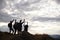 Silhouettes of five young adult friends celebrating at the summit after a mountain hike, back view