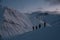 Silhouettes of four skiers climbing a mountain slope at dusk