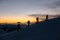 Silhouettes of four skiers with poles reached the highest point after sunset